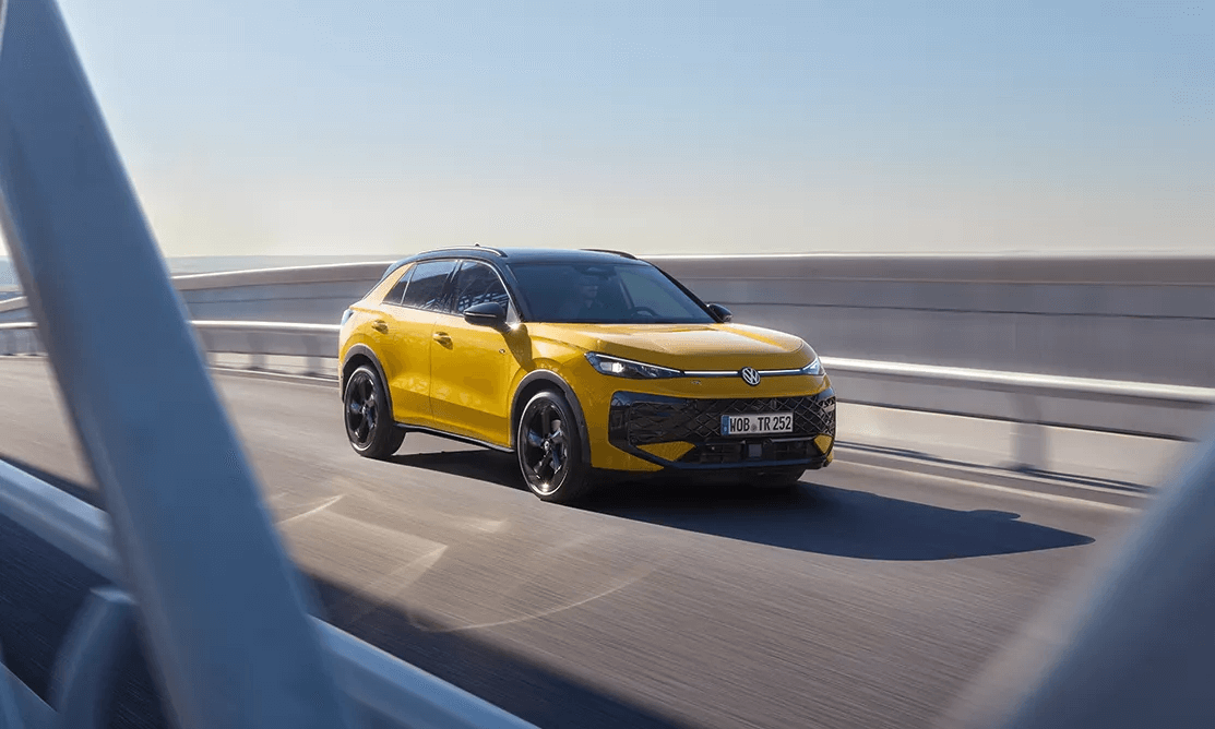 Geltonas „Volkswagen T-Roc“ važiuoja per tiltą saulėtą dieną.