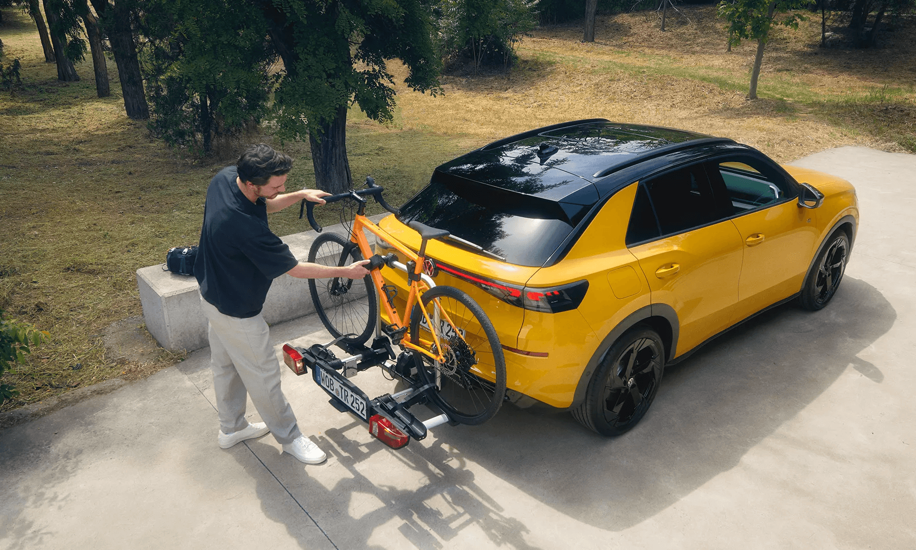 Vyras tvirtina oranžinį dviratį prie „Volkswagen T-Roc“ kablio.