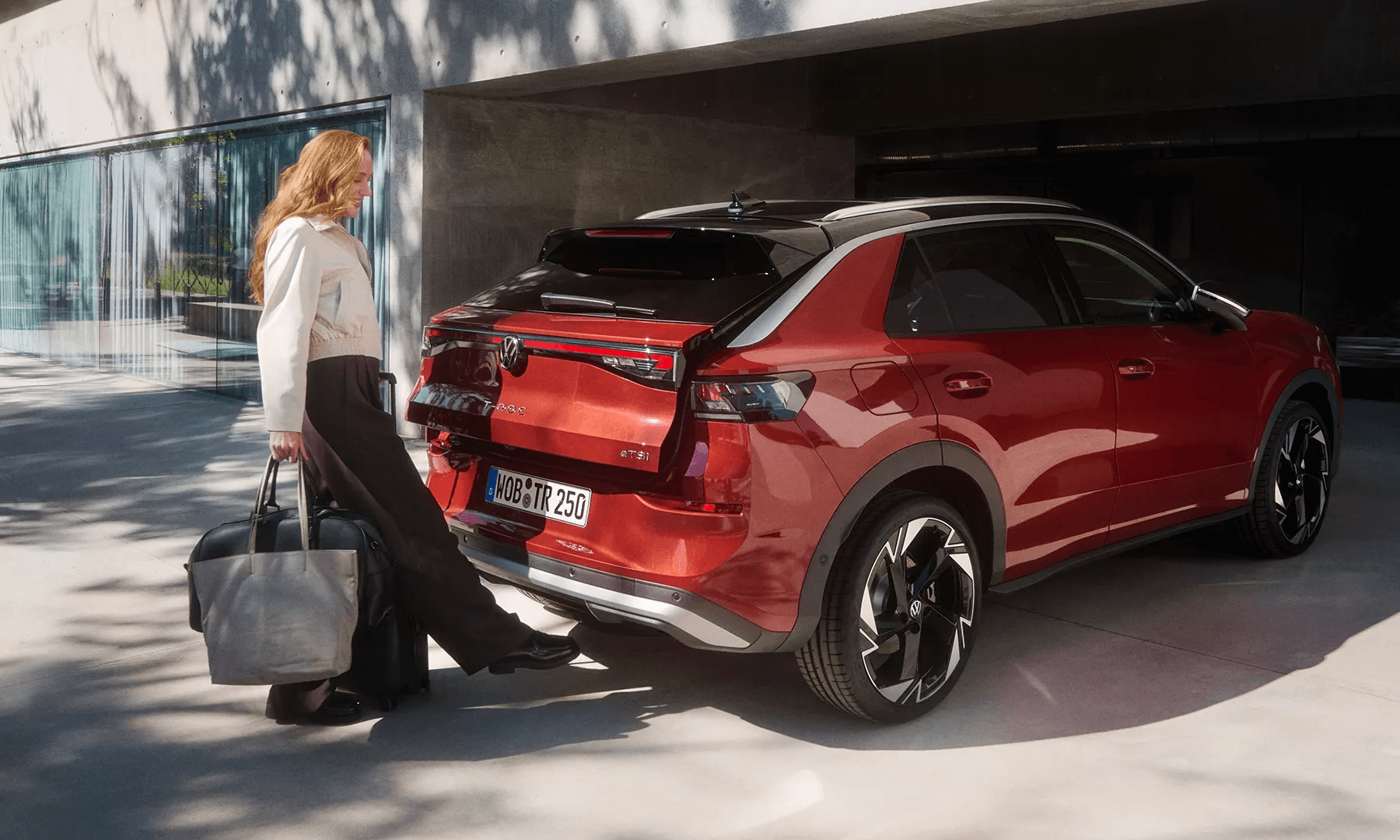 Moteris su bagažu aktyvuoja raudono „Volkswagen T-Roc“ bagažinę be rankų.