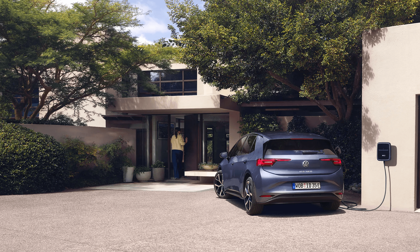 Mėlynas Volkswagen ID.3 elektromobilis važiuoja vingiuotu kalnų keliu su uolėtu peizažu fone.